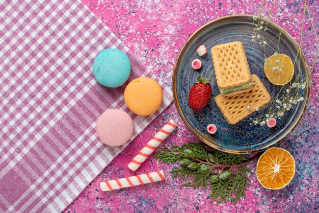 Vista dall'alto di deliziosi waffle con macarons francesi sulla superficie rosa chiaro