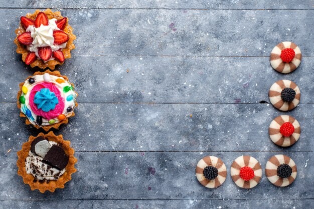 Vista dall'alto di diverse torte con frutta a fette caramelle cioccolato e bacche su grigio, biscotto biscotto dolce zucchero cuocere