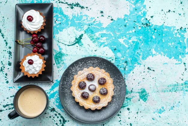 Vista dall'alto di diverse torte con panna e ciliegie fresche su crema dolce da forno azzurra