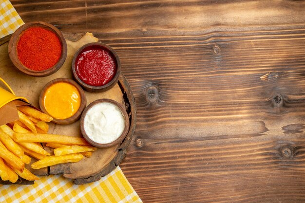 Vista dall'alto di diversi condimenti con patatine fritte su tavola di legno marrone pasto veloce con patate