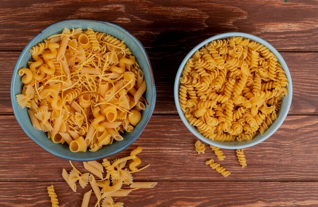 Vista dall'alto di diversi maccheroni e maccheroni rotini in ciotole e su legno