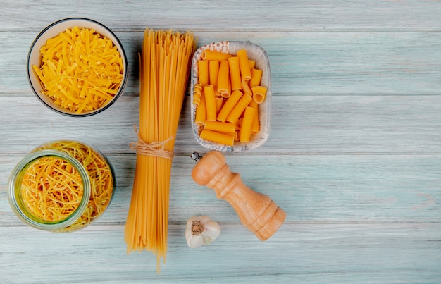 Vista dall'alto di diversi tipi di pasta come tagliatelle spaghetti vermicelli ziti e altri con sale all'aglio sulla superficie in legno con spazio di copia