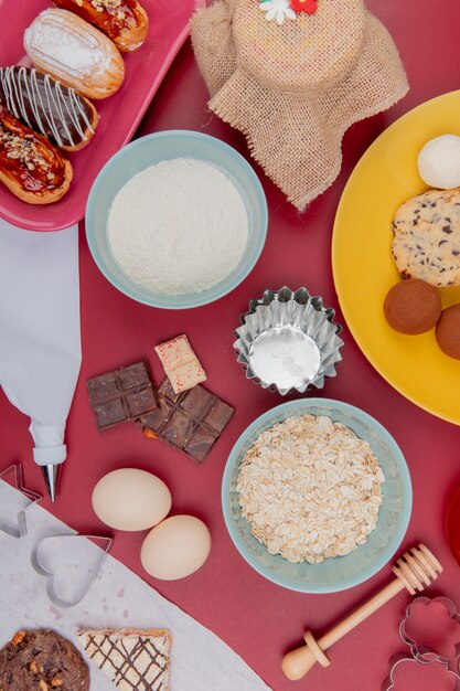 Vista dall'alto di dolci come torta biscotto al cioccolato con uova fiocchi d'avena e farina sul tavolo rosso