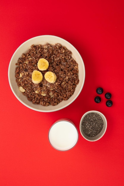 Vista dall'alto di farina d'avena di banana e noce in una ciotola con bicchiere di latte ciotola di semi di chia e bacche di prugnolo su sfondo rosso