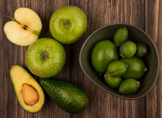 Vista dall'alto di feijoas freschi con lime su una ciotola con mele verdi e avocado isolati su una superficie di legno
