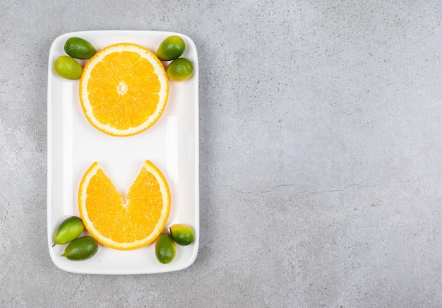 Vista dall'alto di fette d'arancia con kumquat sul piatto bianco.