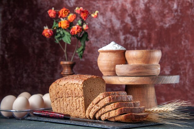 Vista dall'alto di fette di pane nero su vassoio di colore scuro farina farina d'avena grano saraceno su tavola di legno uova su fondo invecchiato di colore misto