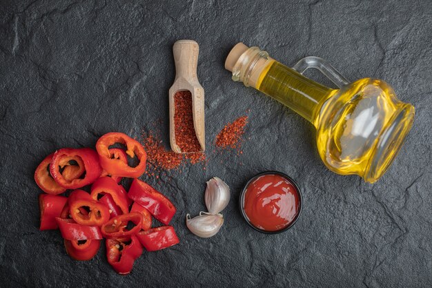 Vista dall'alto di fette di peperone rosso con olio, ketchup e aglio su sfondo nero.
