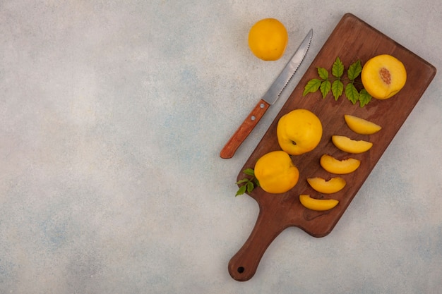 Vista dall'alto di fette di pesche fresche gialle su una tavola da cucina in legno con coltello su uno sfondo bianco con spazio di copia
