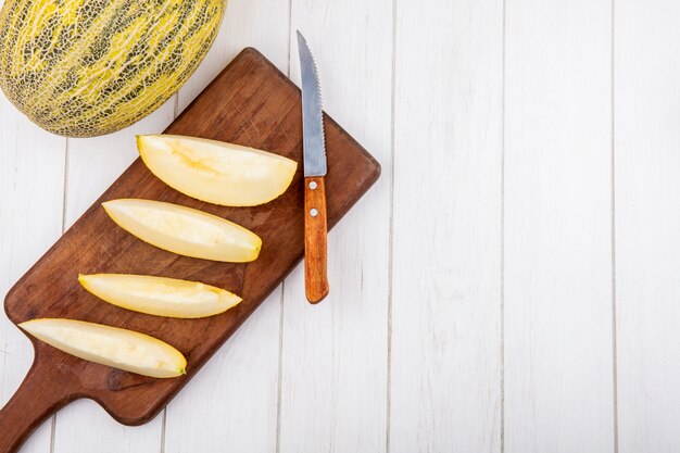 Vista dall'alto di fette fresche di meloni sul bordo della cucina in legno con coltello su legno bianco