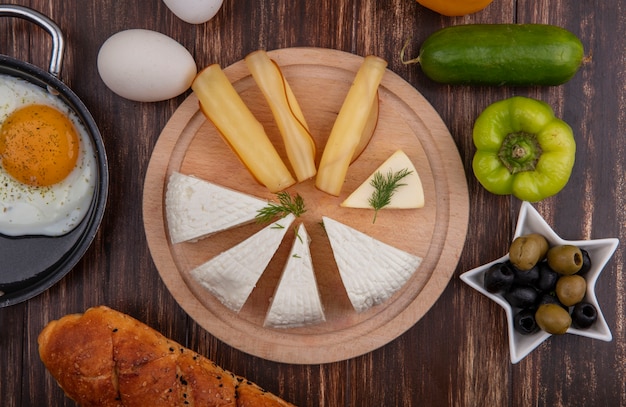 Vista dall'alto di formaggio feta con formaggio affumicato su un supporto con olive, peperoni verdi, cetrioli e uova su uno sfondo di legno