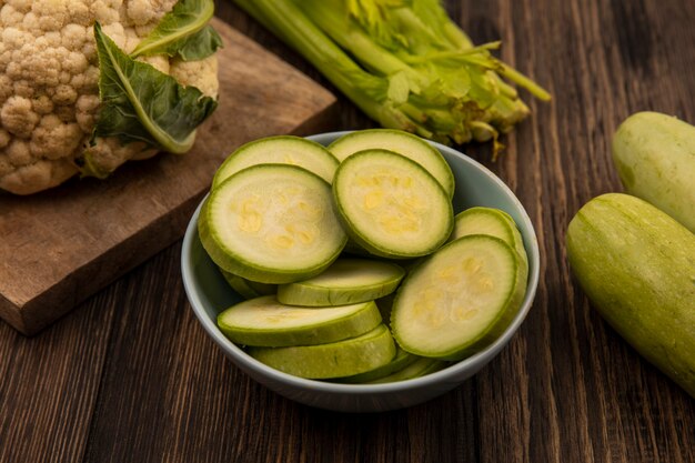 Vista dall'alto di fresche zucchine tritate su una ciotola con sedano zucchine e cavolfiore isolato su una parete in legno