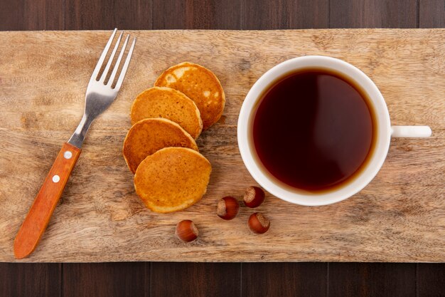 Vista dall'alto di frittelle e tazza di tè con noci e forchetta sul tagliere su fondo in legno