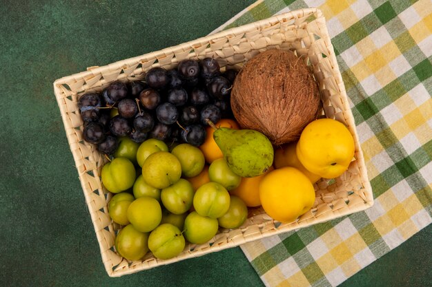 Vista dall'alto di frutta fresca come pesche verde pera e cocco su un secchio su uno sfondo verde