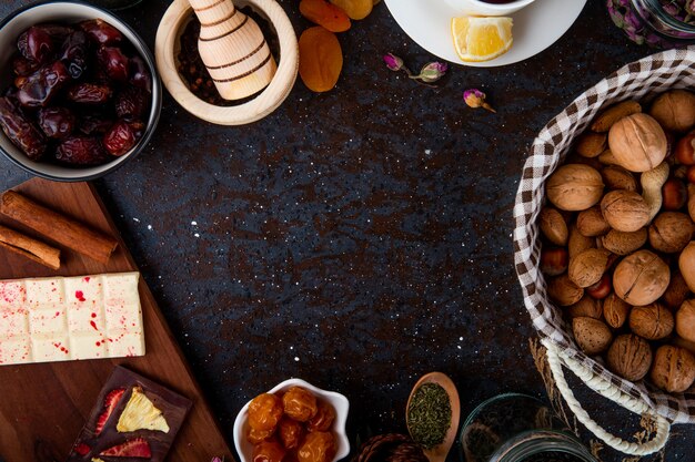 Vista dall'alto di frutta secca con noci, barrette di cioccolato e spezie su fondo nero con copia spazio