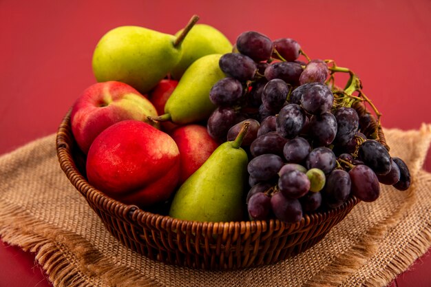 Vista dall'alto di frutti come grapepearpeach su una ciotola di legno su un panno di sacco su uno sfondo rosso