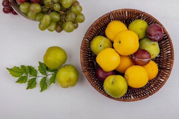 Vista dall'alto di frutti come nectacots pluots nel carrello con uva nella ciotola e pluots verdi su sfondo bianco