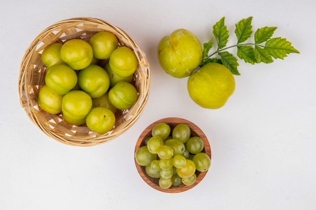 Vista dall'alto di frutti come prugne in cestino e verde pluots con ciotola di acini d'uva bianca su sfondo bianco