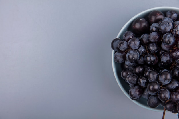 Vista dall'alto di frutti come uva e prugnole nella ciotola su sfondo grigio con spazio di copia