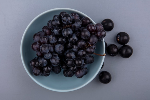 Vista dall'alto di frutti come uva nella ciotola e bacche di prugnole su sfondo grigio