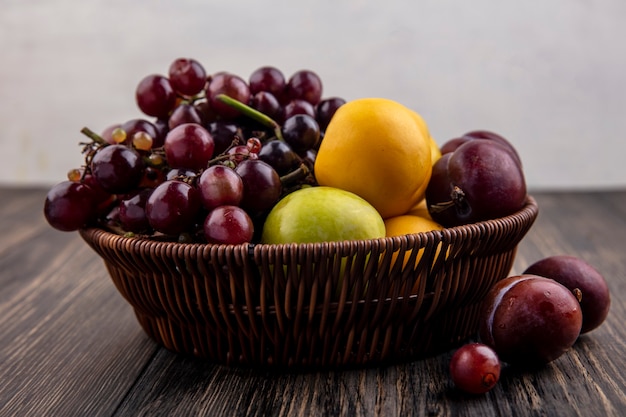 Vista dall'alto di frutti come uva pluots nectacots nel cestello e su una superficie di legno e sfondo bianco