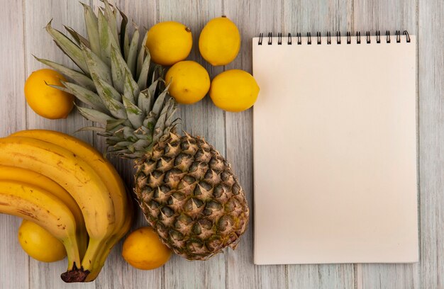 Vista dall'alto di frutti ricchi di vitamine come banane ananas e limoni isolati su uno sfondo di legno grigio con spazio di copia