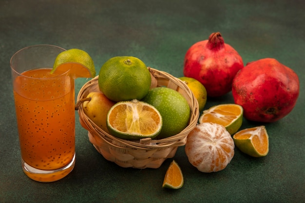 Vista dall'alto di frutti sani come mele pera kiwi su un secchio con succo fresco su un bicchiere con mandarini e melograni isolati