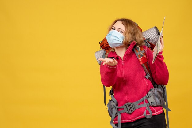 Vista dall'alto di giovane ragazza in viaggio curiosa in mascherina medica raccogliendo i suoi bagagli e tenendo la mappa