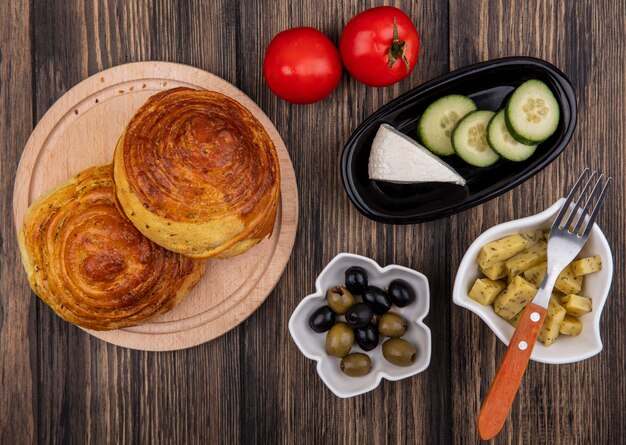 Vista dall'alto di gogals su una tavola da cucina in legno con olive su una ciotola con formaggio bianco e fette di cetriolo su una ciotola nera su uno sfondo di legno