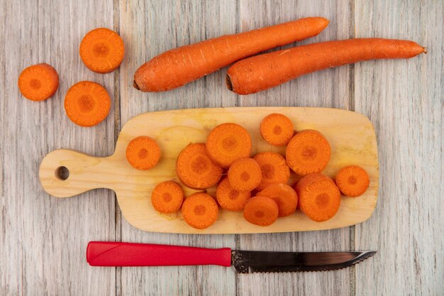 Vista dall'alto di gustose carote tritate su un tagliere di cucina in legno con coltello con carote isolato su una superficie di legno grigia