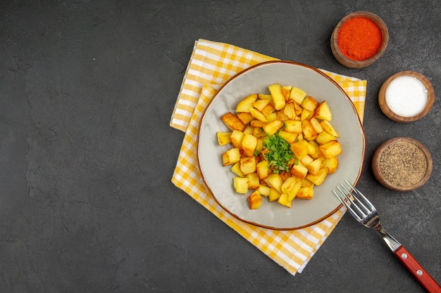 Vista dall'alto di gustose patate fritte all'interno del piatto con condimenti sulla superficie grigio scuro