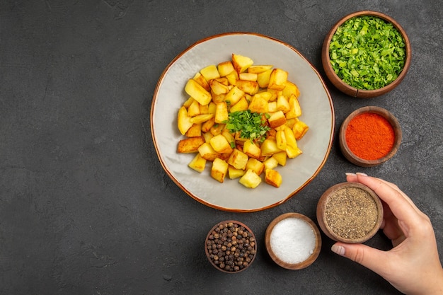 Vista dall'alto di gustose patate fritte all'interno del piatto con condimenti sulla superficie scura