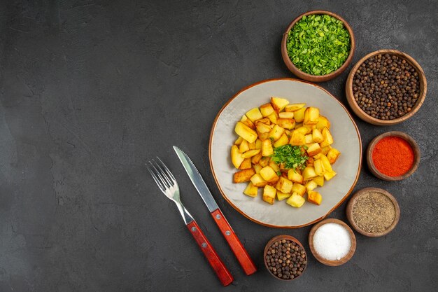 Vista dall'alto di gustose patate fritte all'interno del piatto con verdure e condimenti sulla superficie scura