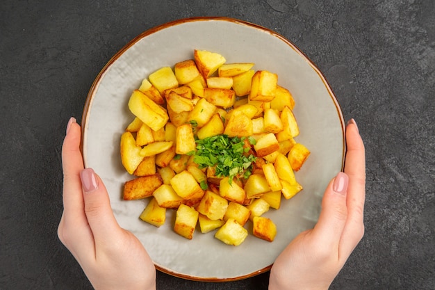 Vista dall'alto di gustose patate fritte all'interno del piatto con verdure sulla superficie scura