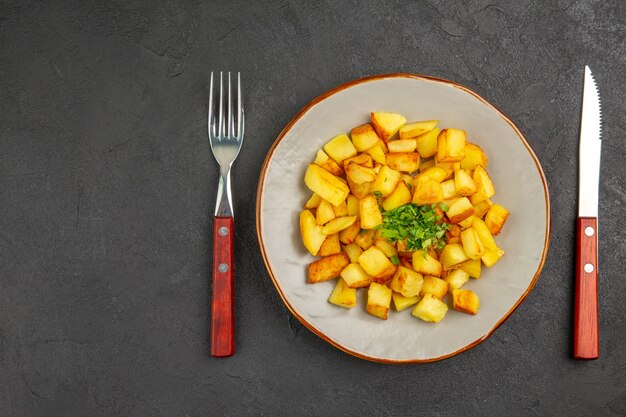 Vista dall'alto di gustose patate fritte all'interno del piatto con verdure sulla superficie scura