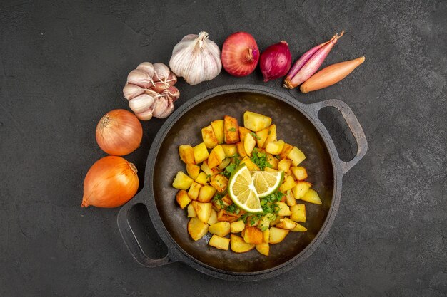 Vista dall'alto di gustose patate fritte all'interno della padella con limone e garlics intorno sulla superficie scura