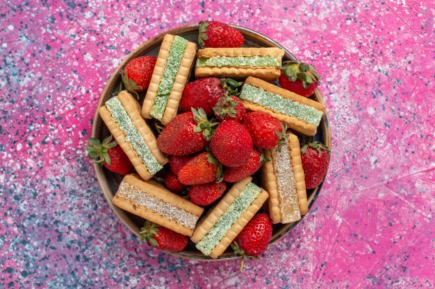 Vista dall'alto di gustosi biscotti waffle con fragole rosse sulla superficie rosa