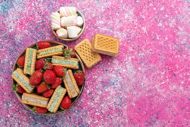 Vista dall'alto di gustosi biscotti waffle con marshmallow e fragole rosse fresche sulla superficie rosa