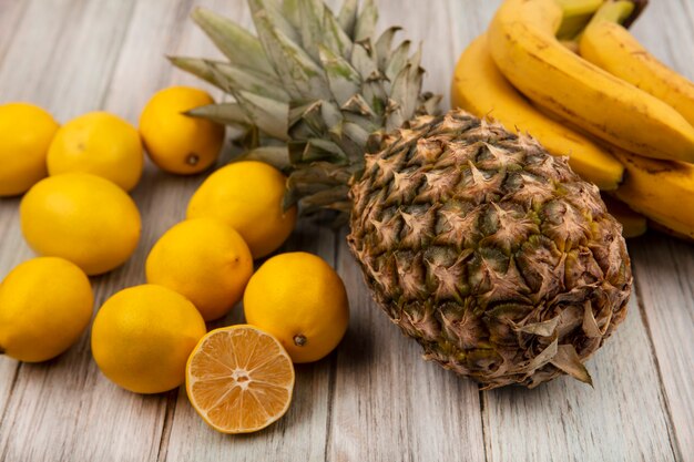 Vista dall'alto di gustosi frutti come ananas, banane e limoni isolati su una superficie di legno grigia