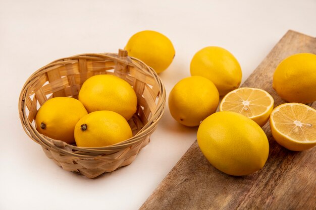 Vista dall'alto di gustosi limoni su un secchio con limoni isolato su una tavola di cucina in legno su un muro bianco