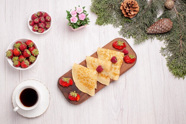 Vista dall'alto di gustosi pancake dolci con frutti di bosco e tazza di tè su bianco