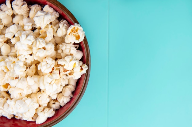 Vista dall'alto di gustosi popcorn su una ciotola di legno sulla superficie del blu