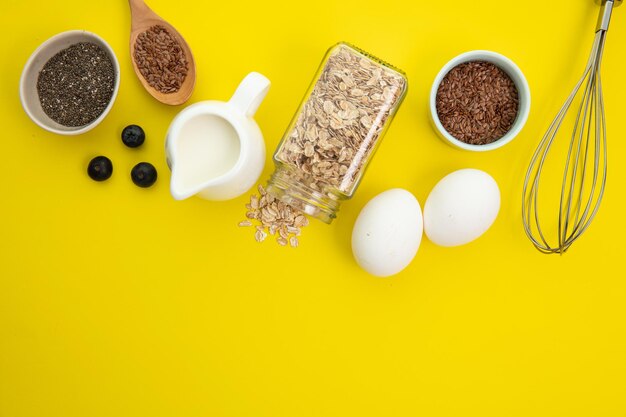 Vista dall'alto di ingredienti come avena di chia e semi di lino latte uovo di prugnolo per fare la farina d'avena con frusta su sfondo giallo