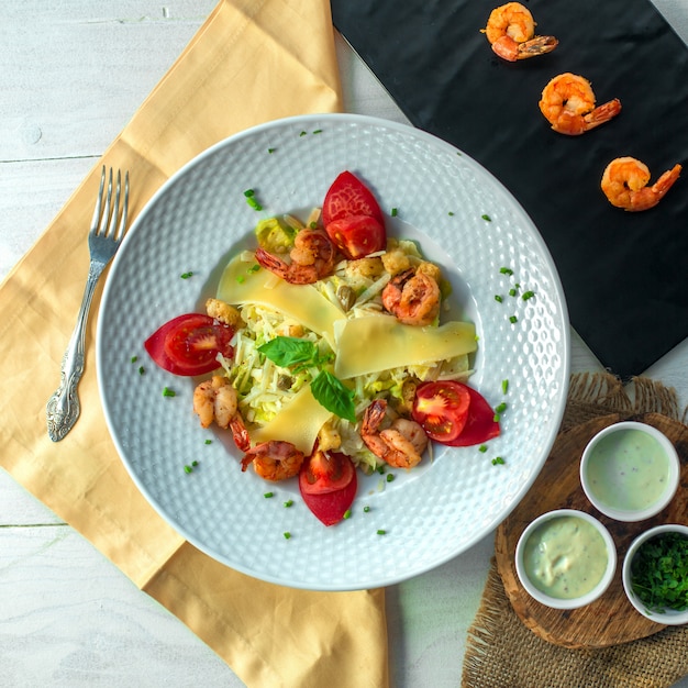 Vista dall'alto di insalata di gamberi con formaggio e pomodori su un piatto bianco