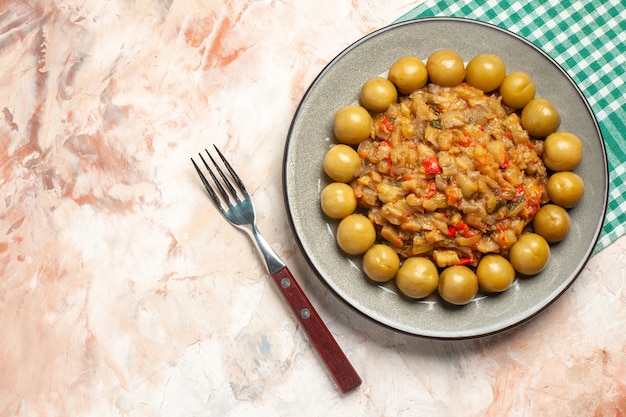 Vista dall'alto di insalata di melanzane arrosto e prugne sottaceto sulla piastra sulla forcella tovagliolo a scacchi bianco turchese sulla superficie nuda