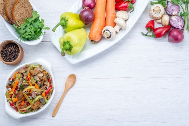 Vista dall'alto di insalata di verdure fresche a fette con carne insieme a pagnotte di pane e verdure intere e verdi su luce, insalata di farina alimentare vitamina