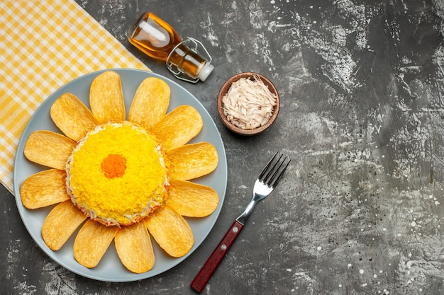 Vista dall'alto di insalata sul lato sinistro con tovagliolo giallo sotto di esso con bottiglia di olio forchetta formaggio sul lato sul tavolo grigio scuro