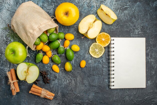 Vista dall'alto di kumquat freschi all'interno e all'esterno di una piccola borsa bianca caduta accanto a fette di limone e mela lime alla cannella su sfondo grigio