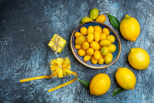 Vista dall'alto di kumquat organici su un piatto blu limoni freschi con foglie e scatole regalo gialle su sfondo scuro