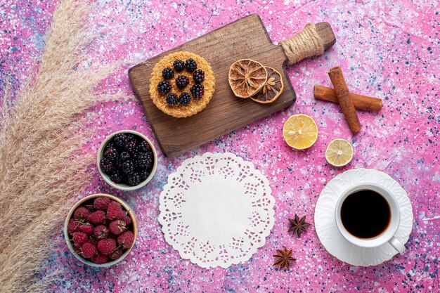 Vista dall'alto di lamponi e more all'interno di piccole pentole con tazza di tè alla cannella sulla superficie rosa chiaro